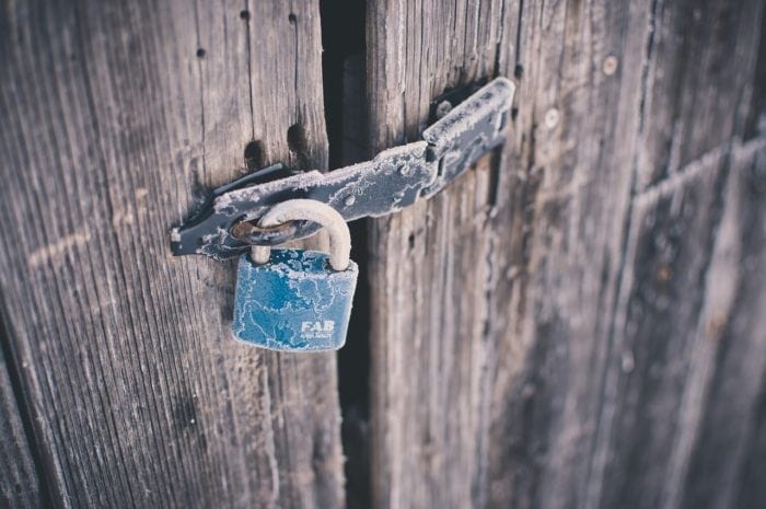 Padlock on wooden door that's frozen over with frost that prevents accessibility to the other side