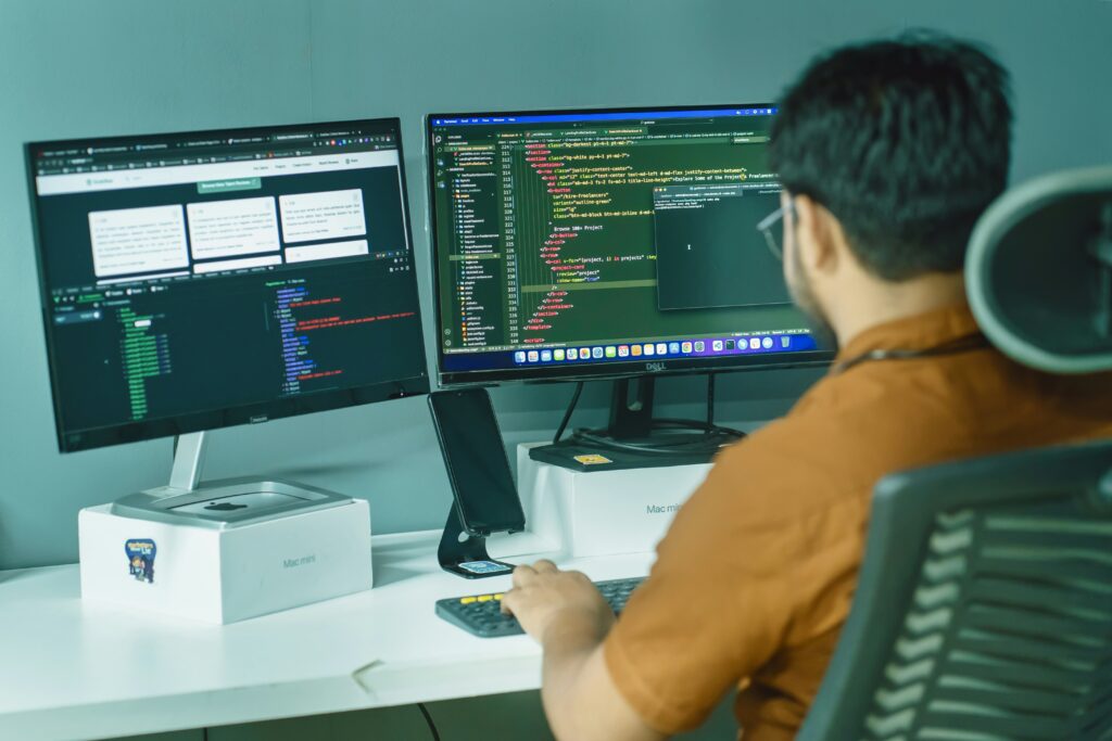 Back of a person sitting at a desk, using two computer monitors while working.