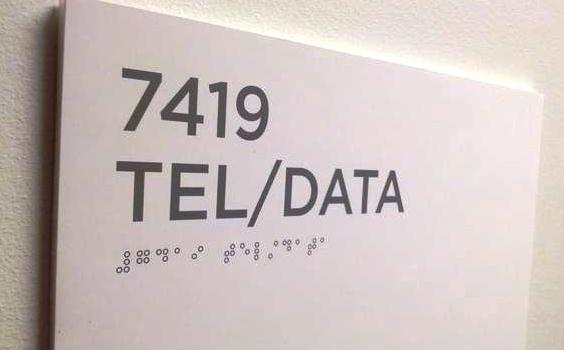 Image showing an office sign with a room number in print and printed-braille. The braille is flat and unreadable.